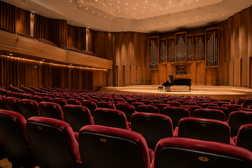 Leerer Konzertsaal mit roten Samtsesseln, Flügel auf der Bühne und großer Orgel